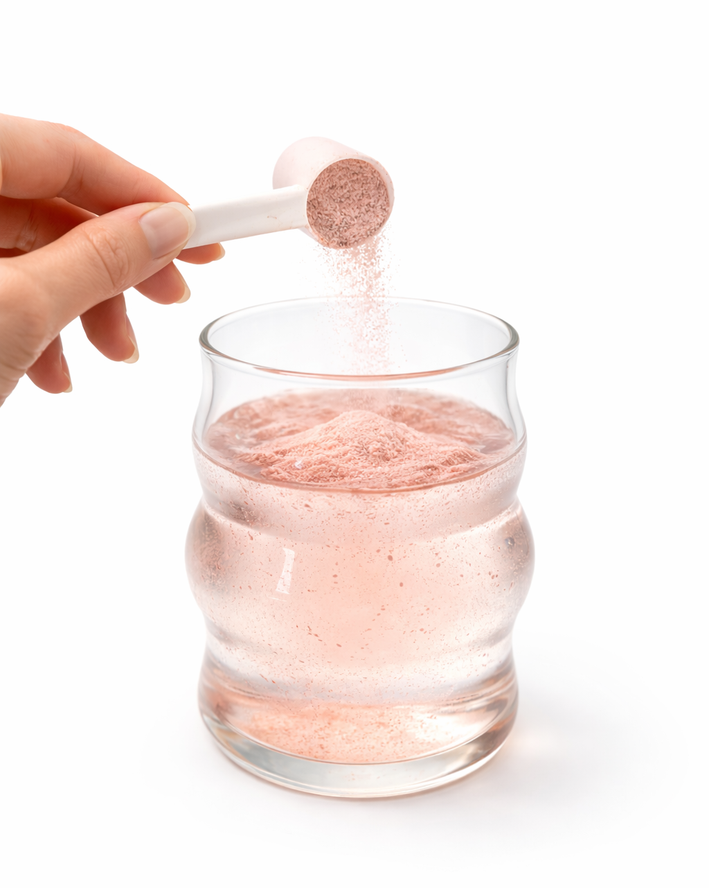 Hand adding a pink powder from a scoop into a glass of water on a white background