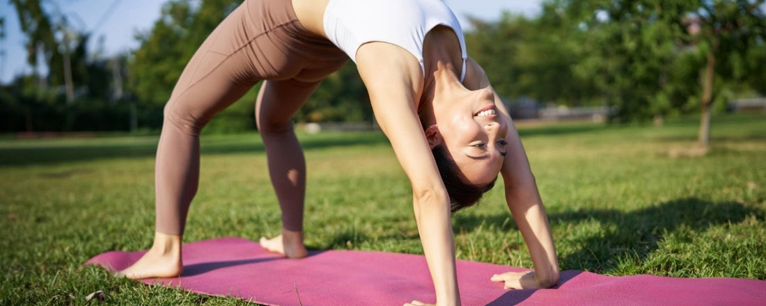 Woman practicing yoga outdoors on a pink mat in downward dog pose, promoting movement and mindfulness for hormone balance and wellbeing.