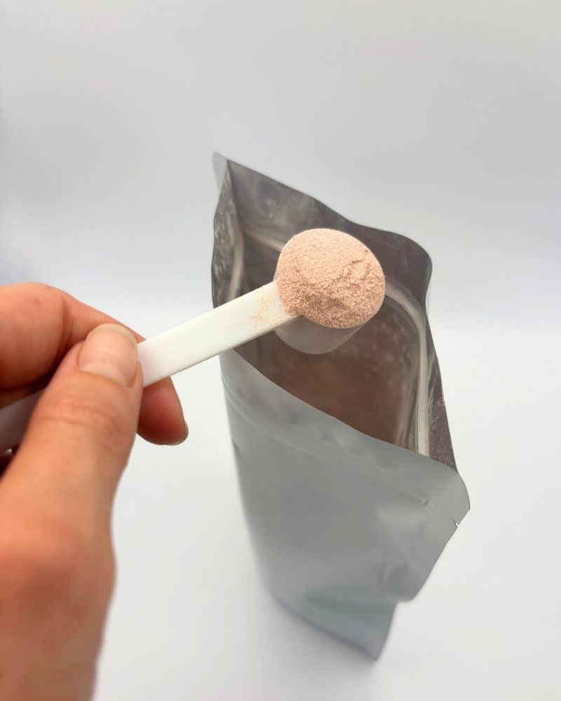 Hand holding a white stick with a custom skin glow powder over a gray pouch on a light gray background