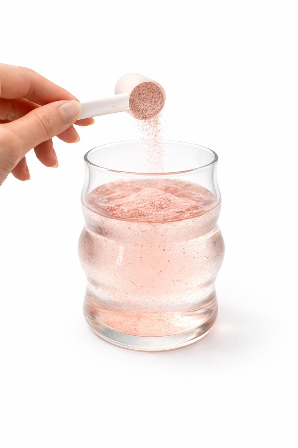 Hand adding a pink powder from a scoop into a glass of water on a white background