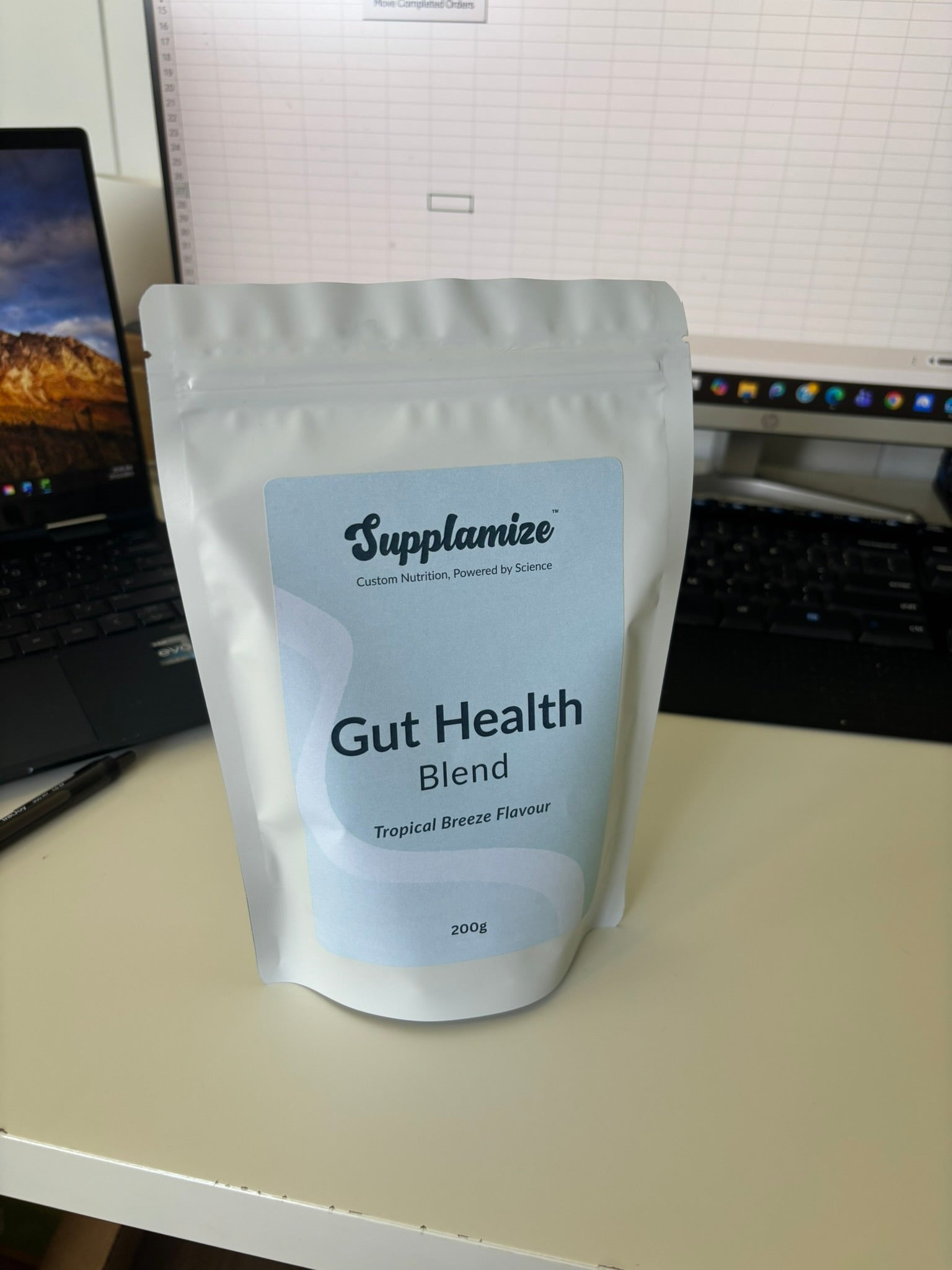 Supplement package labeled 'Gut Health Blend' by Supplamize on a desk with a computer in the background.